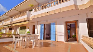 Un edificio de dos pisos con un balcón, una terraza con mesa y sillas, y una puerta que da a una habitación interior.