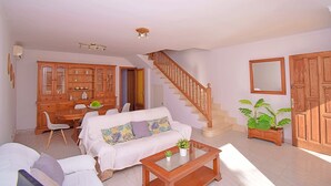 Amplia sala de estar con sofá, mesa de centro y aparador de madera. Una escalera conduce a otro nivel, y se observa una planta en maceta.