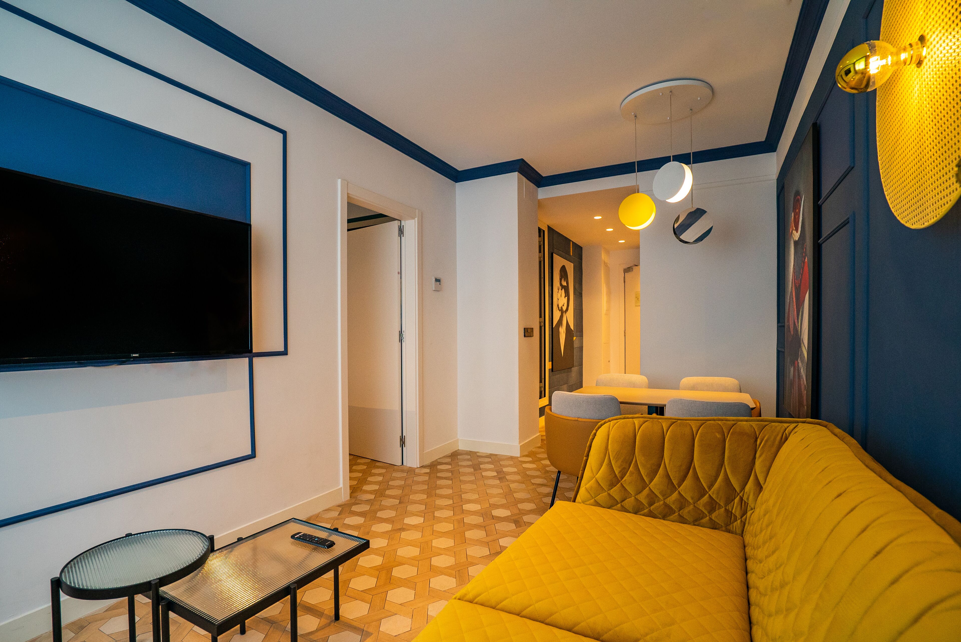 Una sala de estar moderna con un televisor de pantalla plana grande, un sofá amarillo, una mesita y un suelo con diseño.