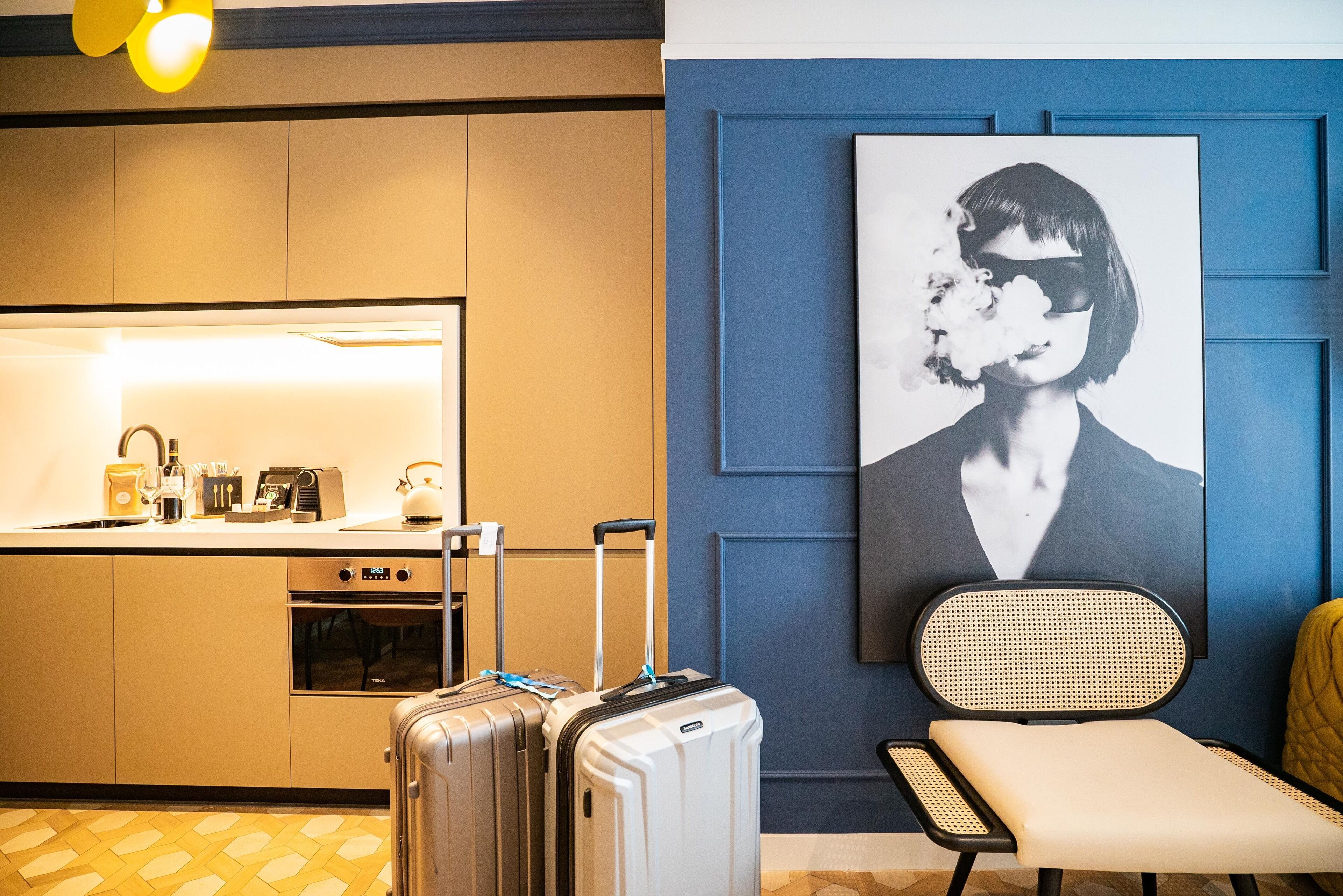 Ein Hotelzimmer mit einer Küchenzeile, einer Sitzecke mit einem Sessel und einem großen Poster an der Wand.