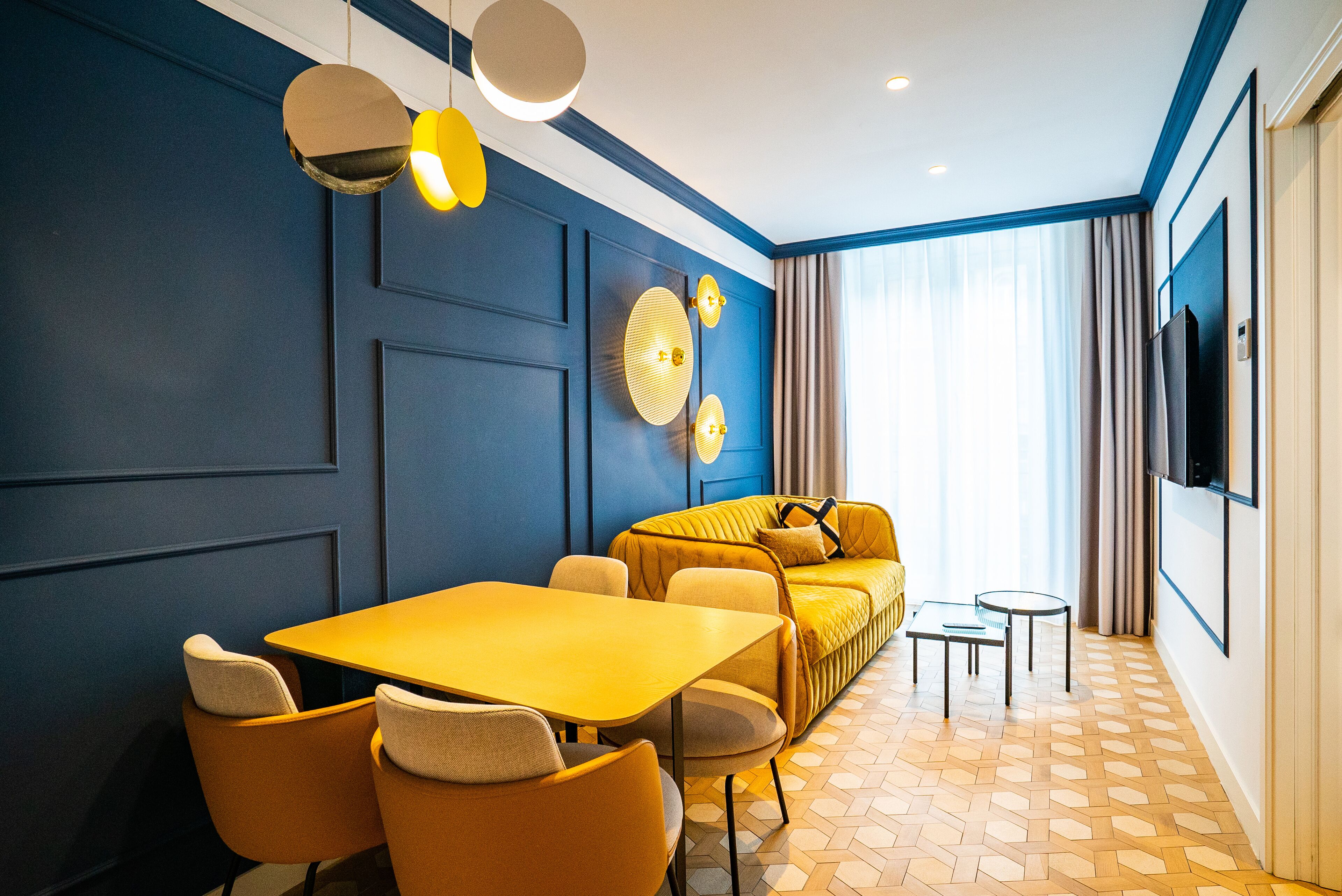 Ein modernes Hotelzimmer mit gelbem Tisch und Stühlen, einer Couch, einem Fernseher und einem gestreiften Boden.