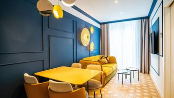 Ein modernes Hotelzimmer mit gelbem Tisch und Stühlen, einer Couch, einem Fernseher und einem gestreiften Boden.