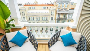Un balcón con sillas y cojines de mimbre, con vistas a una hilera de edificios históricos.
