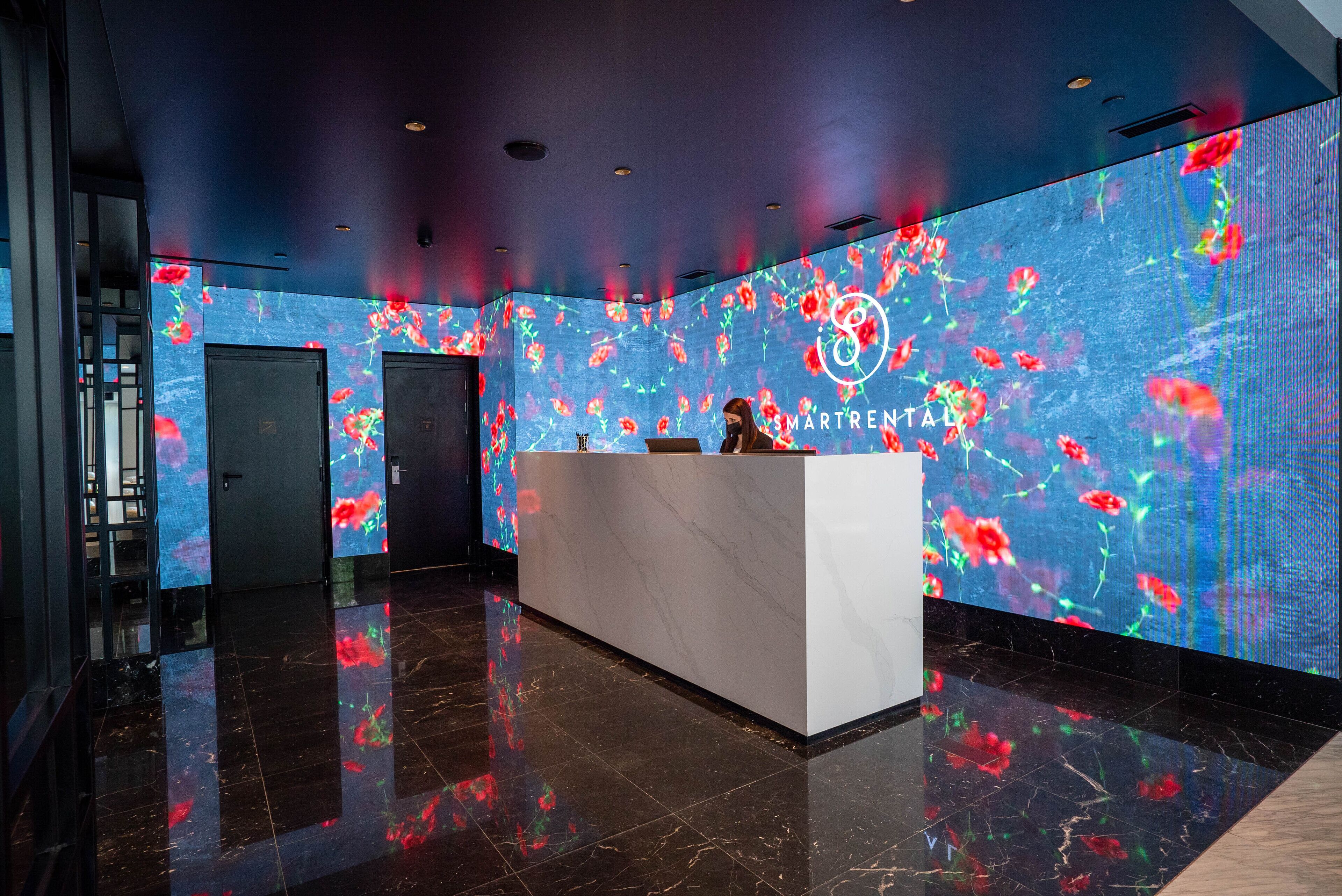 A modern reception area with a marble reception desk, a digital floral display on the walls, and a dark polished floor.