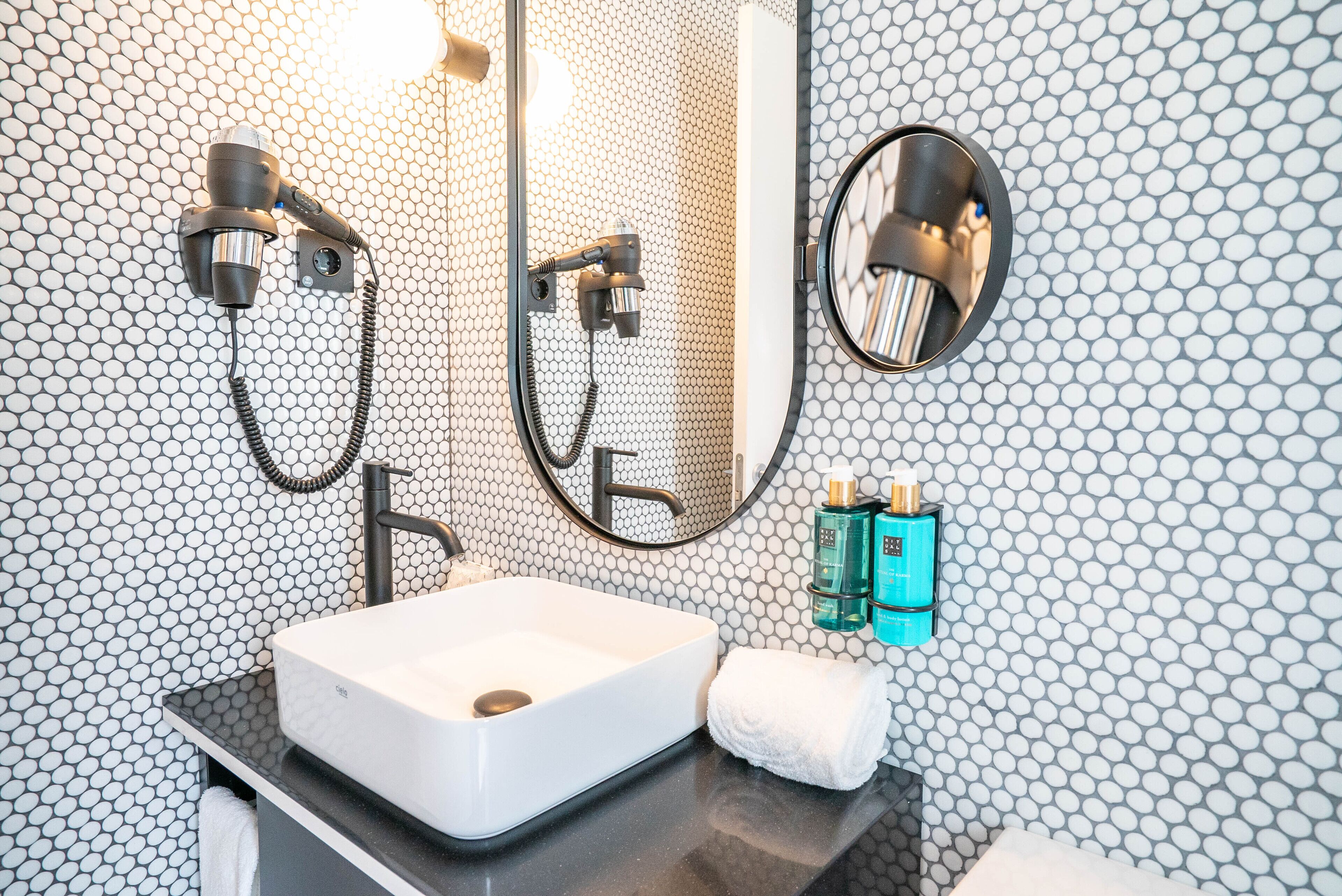 Un baño con lavamanos blanco, espejo, toalla y ducha con cabezal de ducha manual.