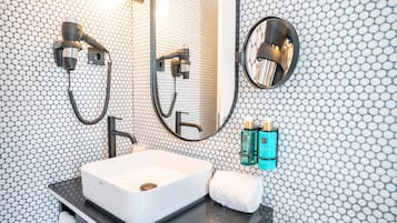 Un baño con lavamanos blanco, espejo, toalla y ducha con cabezal de ducha manual.
