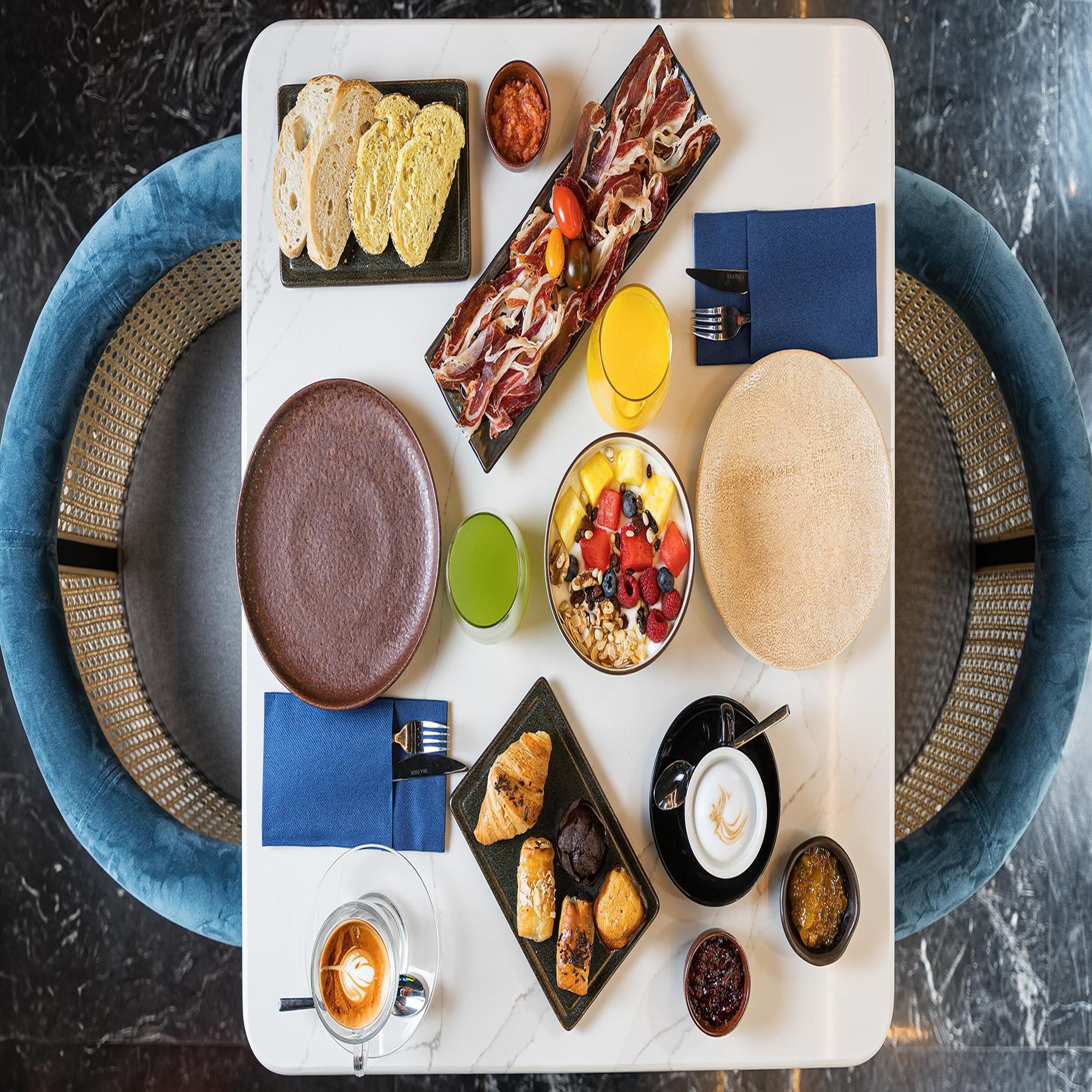 A breakfast tray with bread, meats, fruits, a bowl of yogurt, a croissant, and a coffee cup.