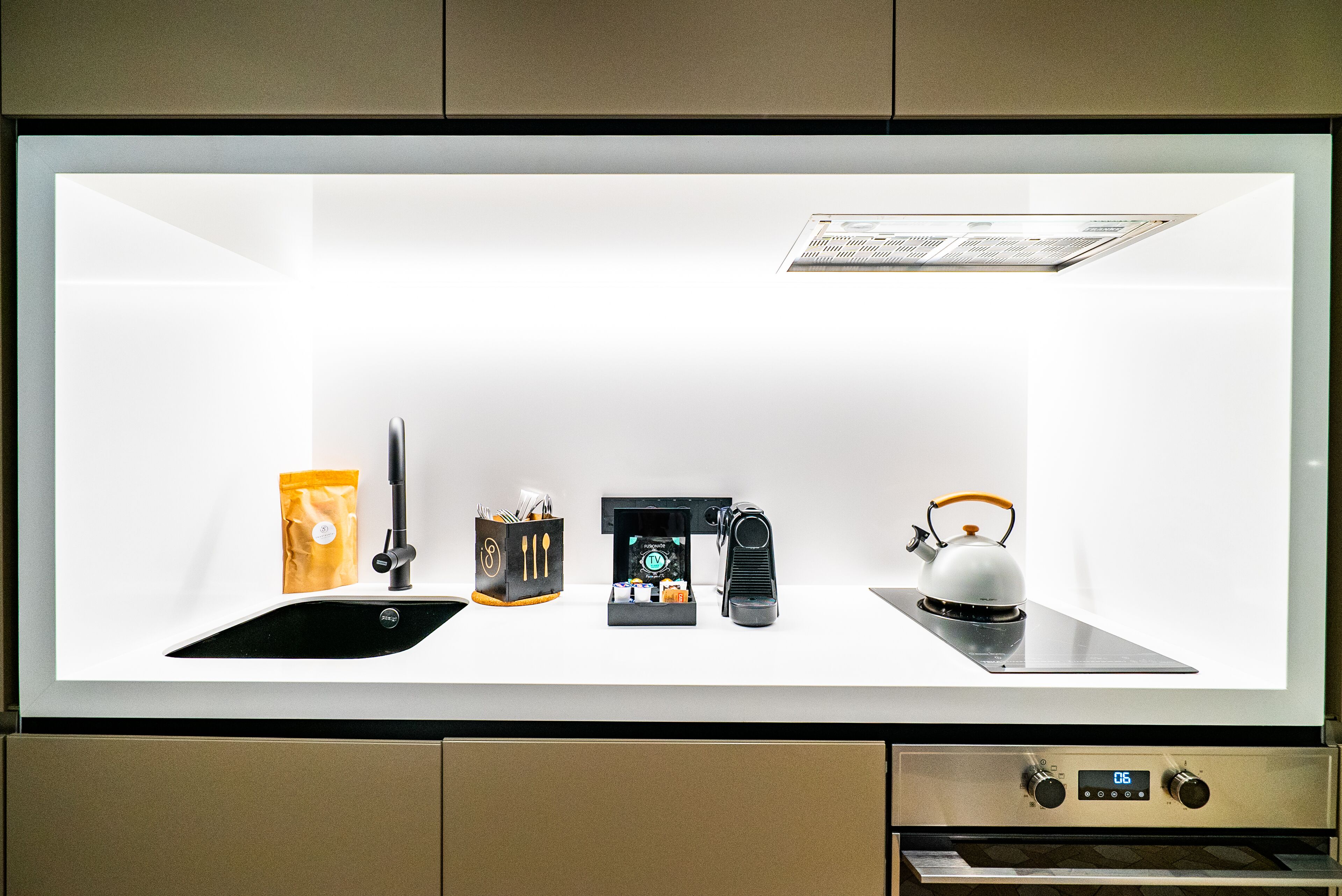 A kitchen with a modern design, featuring a sink, coffee machine, kettle, and a cabinet.