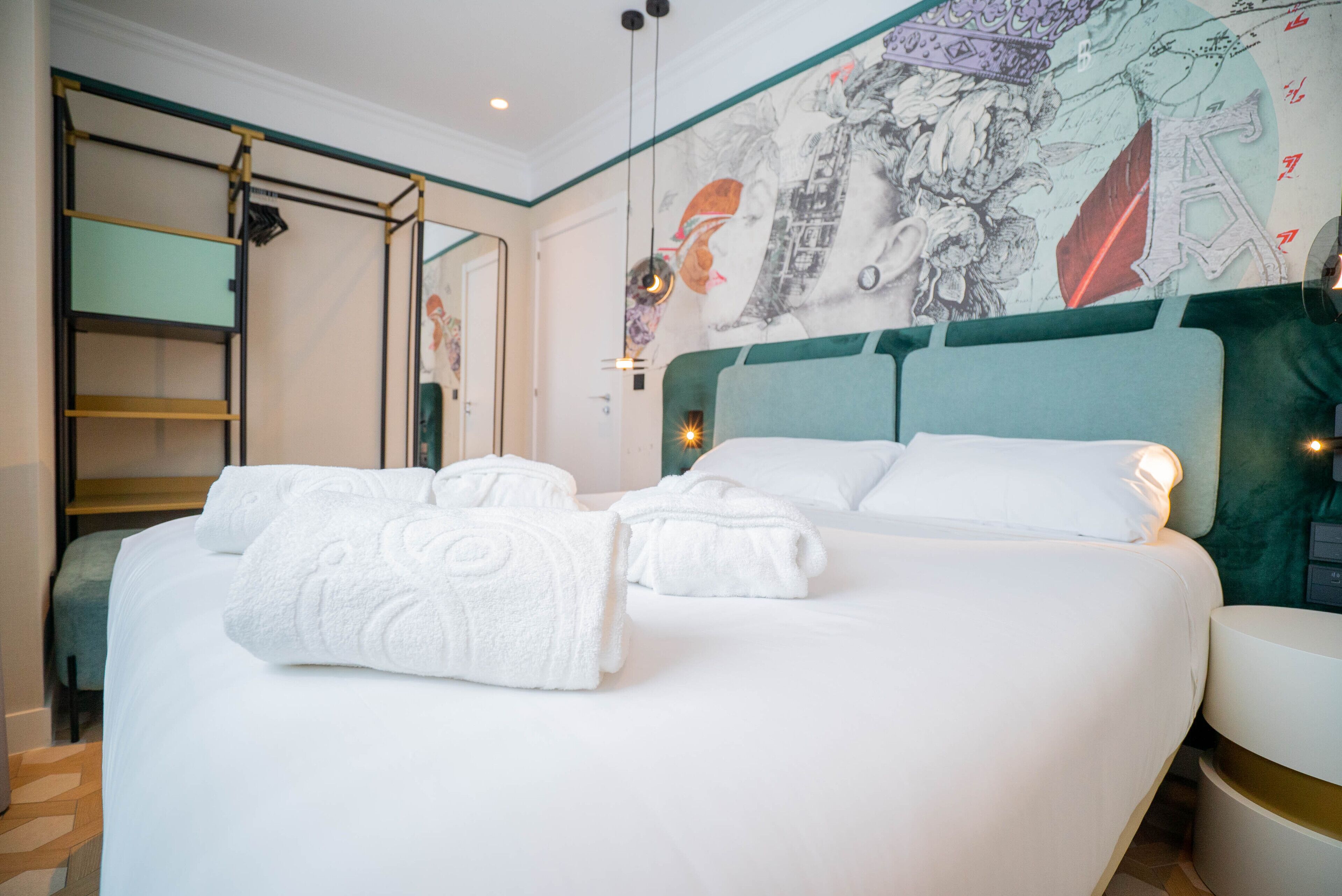 Habitación de hotel con una cama grande, cabecera decorada con obras de arte, armario y espejo.