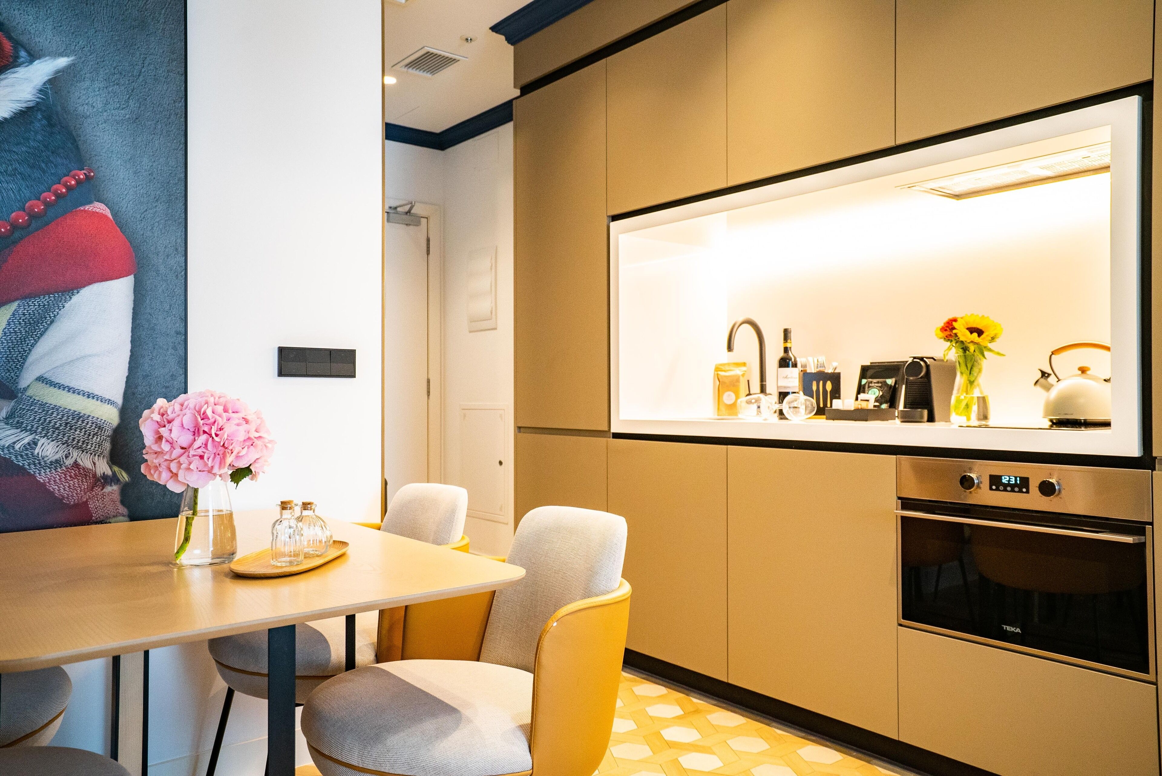 Una cocina moderna con horno empotrado, zona de comedor con mesa y sillas, y una lámpara fijada a la pared sobre la encimera.