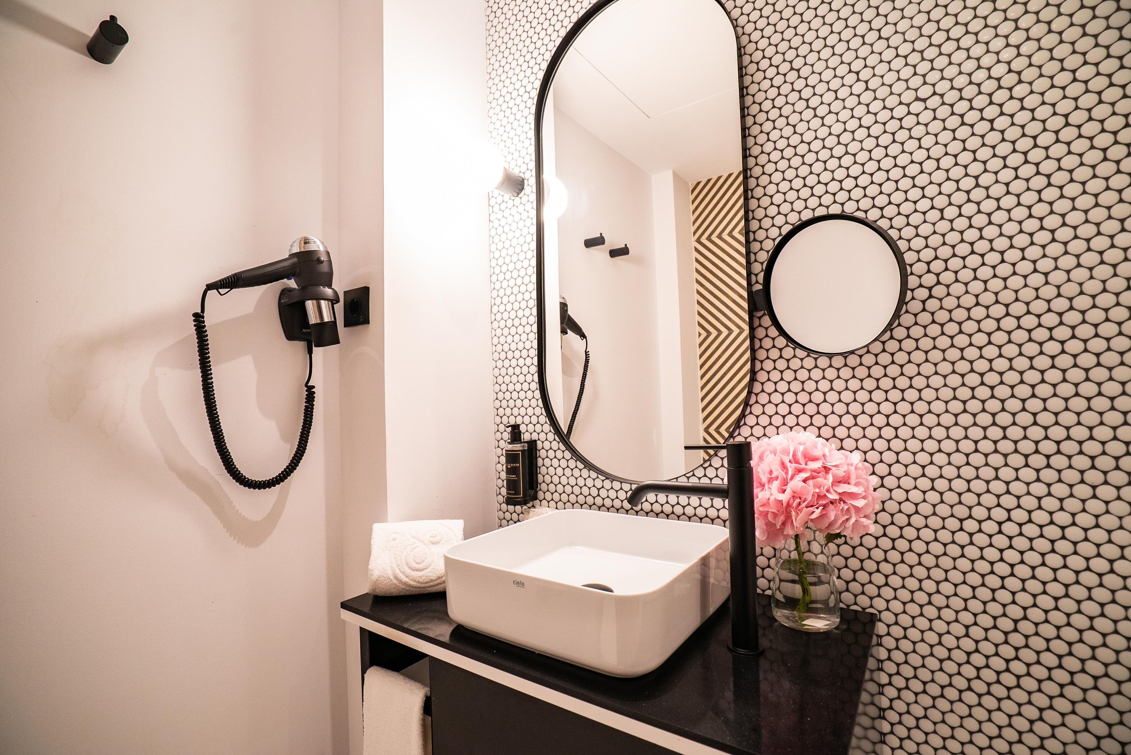 A bathroom with a white sink, black countertop, and a mirror with a hexagonal patterned wall.