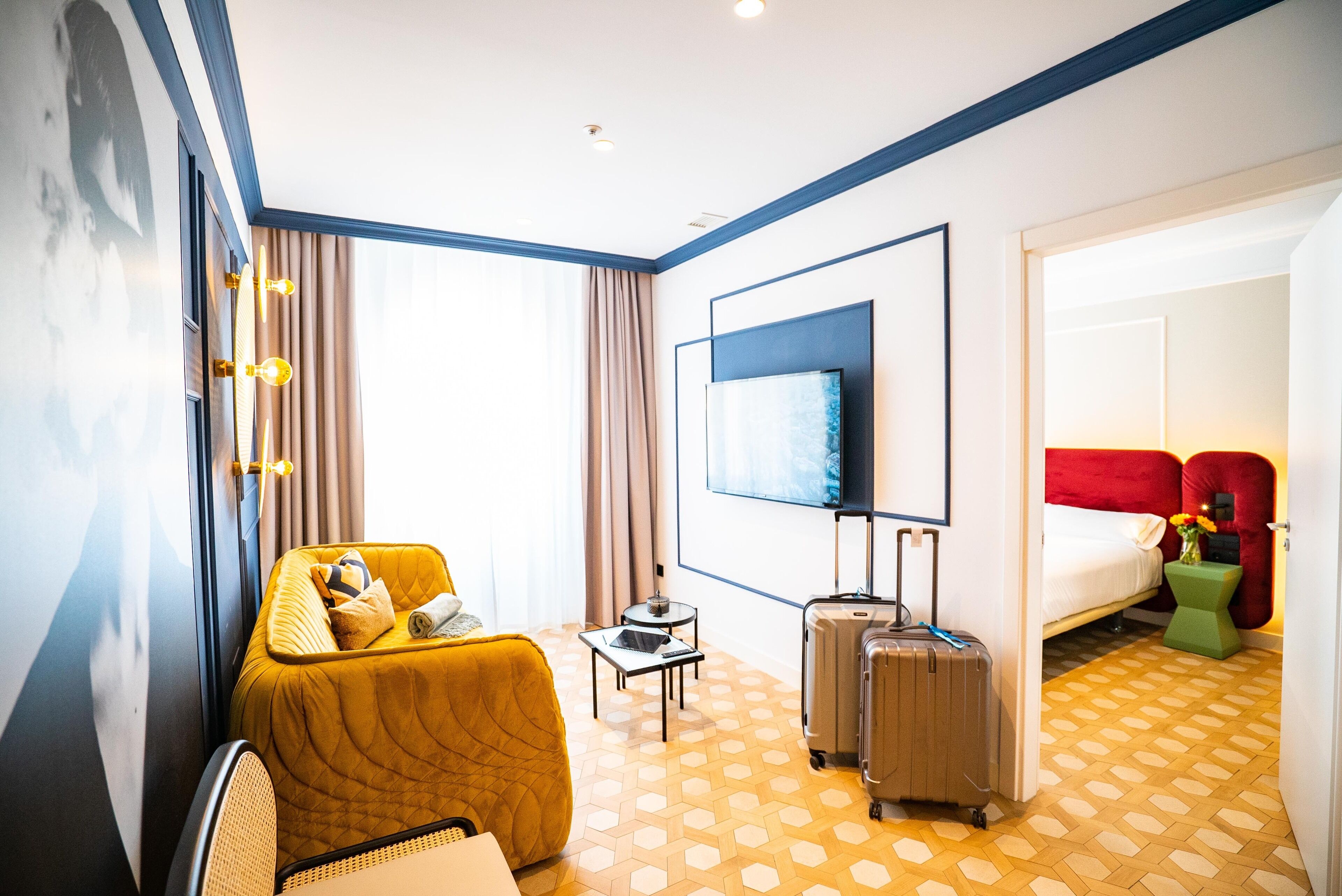 Una habitación de hotel con cama, sofá, televisión, una mesita y una maleta.