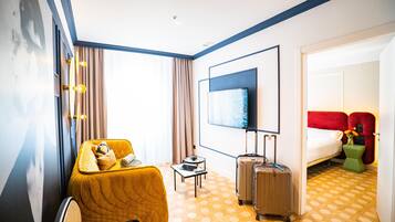 Una habitación de hotel con cama, sofá, televisión, una mesita y una maleta.