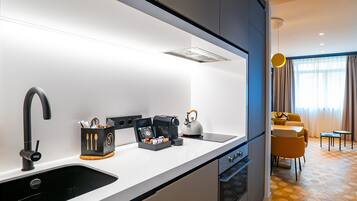 A modern kitchen with a black sink, a coffee machine, and a kettle. There is a dining area with a yellow sofa and a small table.