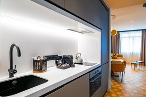 Una cucina moderna con un lavello nero, una macchina da caffè e un bollitore. C'è un'area pranzo con un divano giallo e un tavolino.