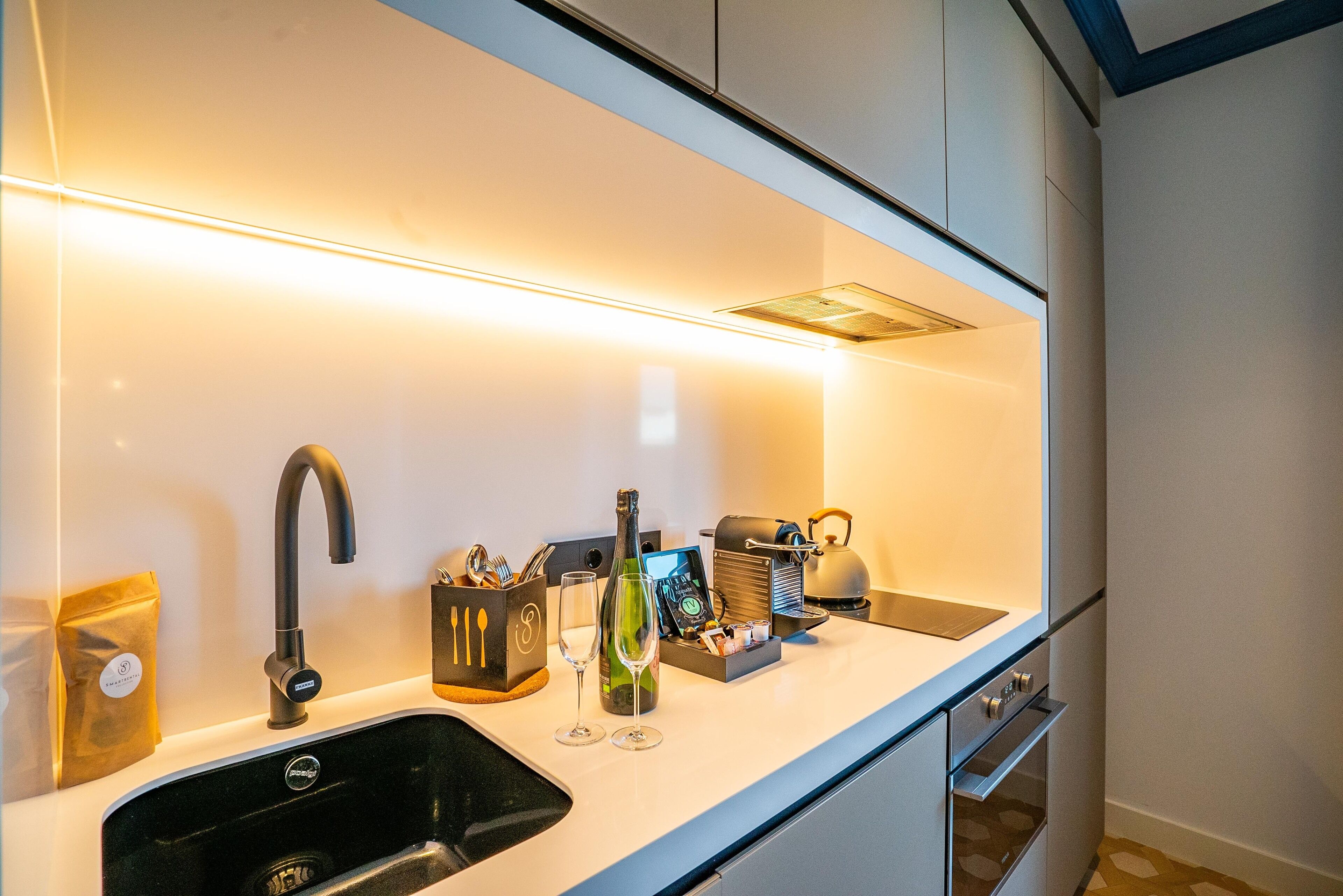 Una cocina moderna con un lavamanos negro, una copa de vino, una botella y una cafetera.