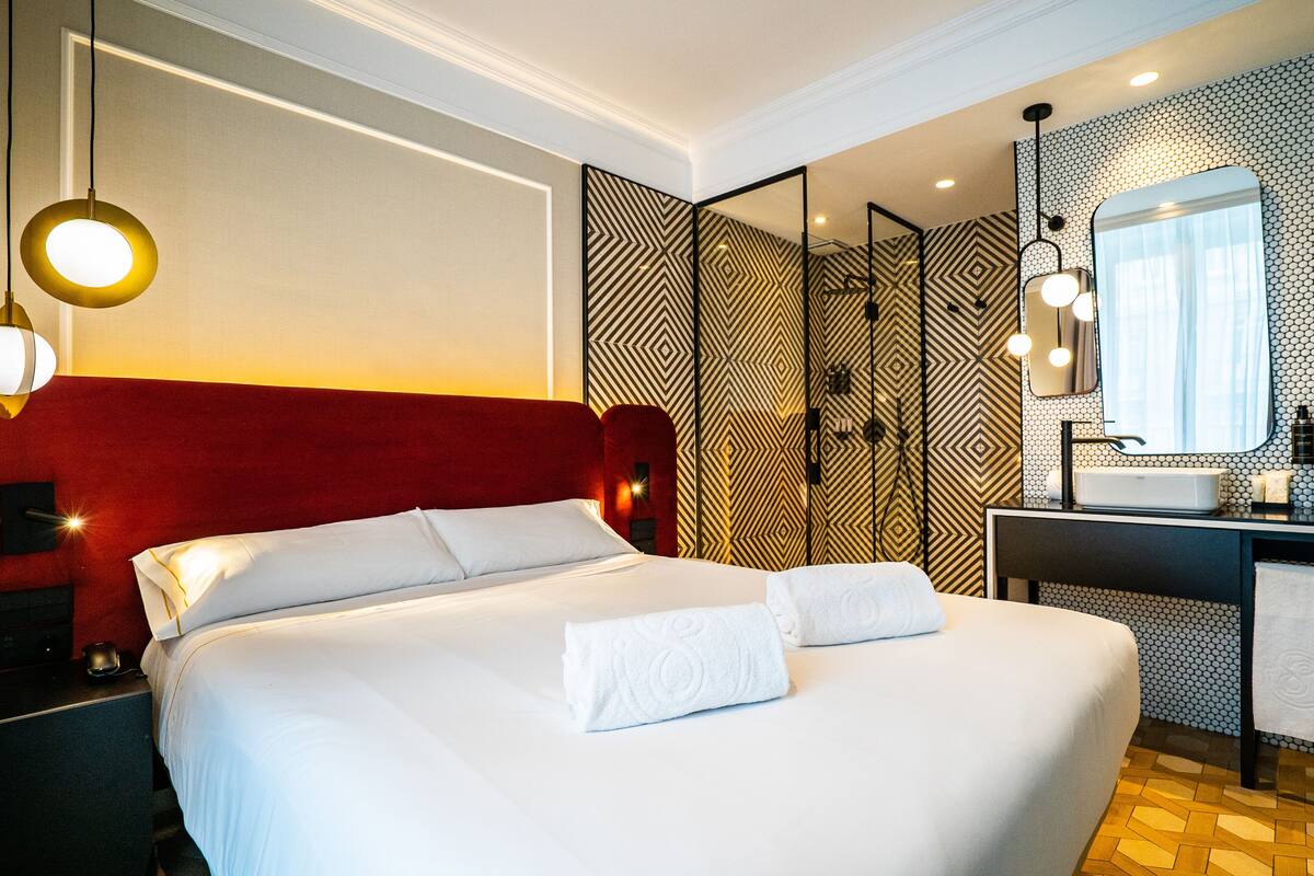 A hotel room with a large bed, a desk with a mirror, and a bathroom with a sink.
