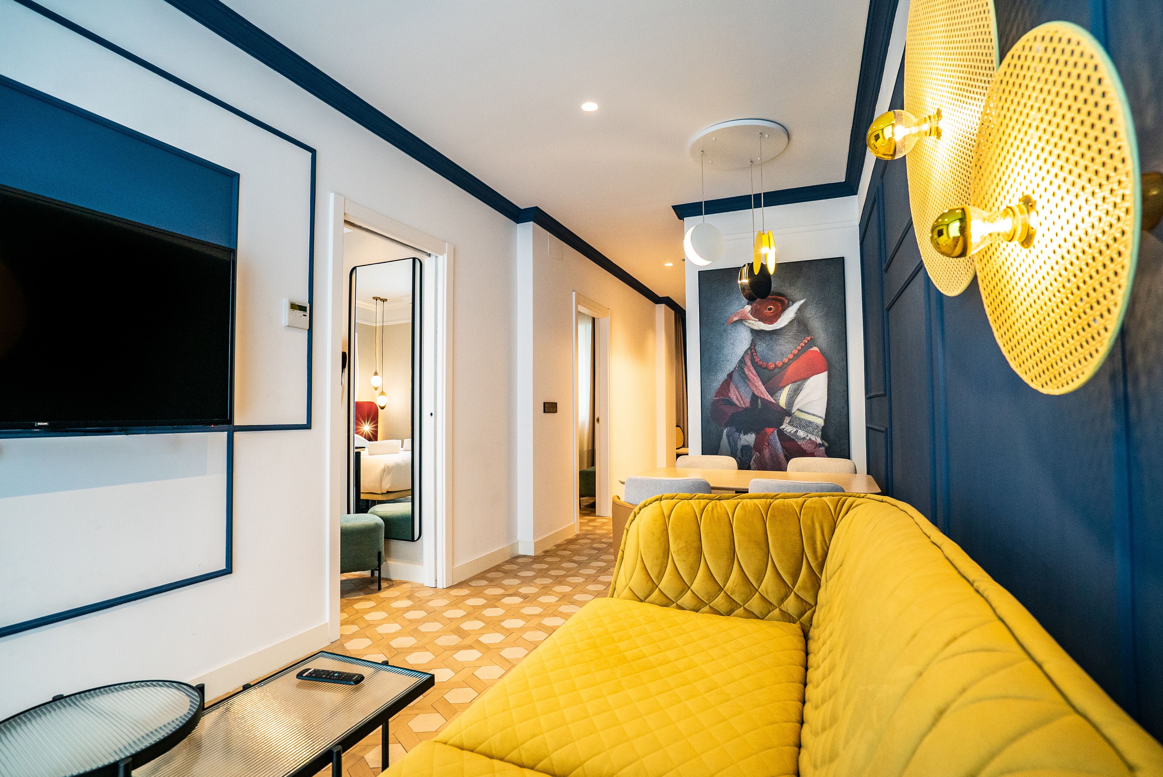 Un salon moderne avec un canapé jaune, un téléviseur à écran plat fixé au mur et un luminaire mural original.