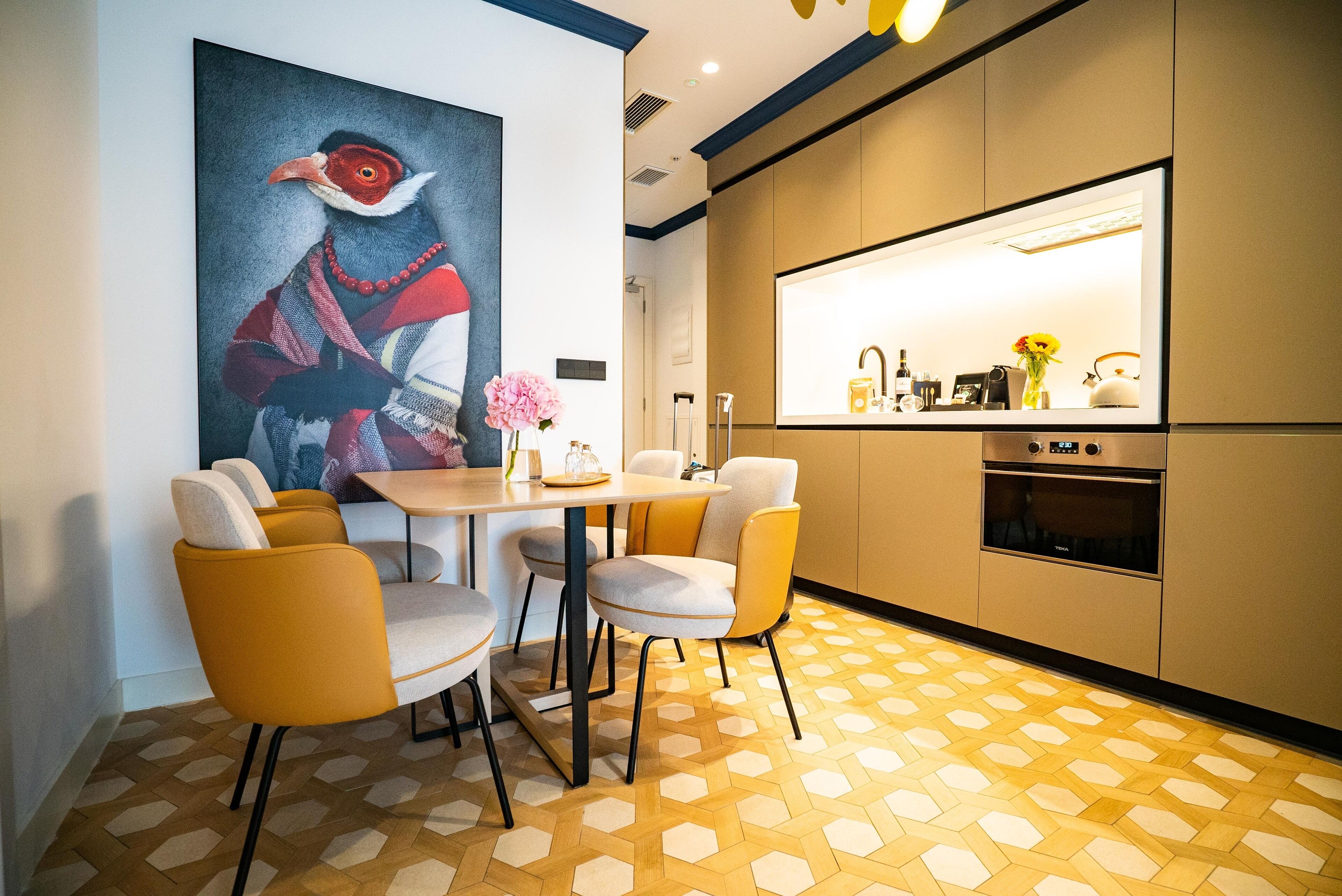 A modern kitchen with a central island, a dining area with yellow chairs, and a large abstract painting on the wall.