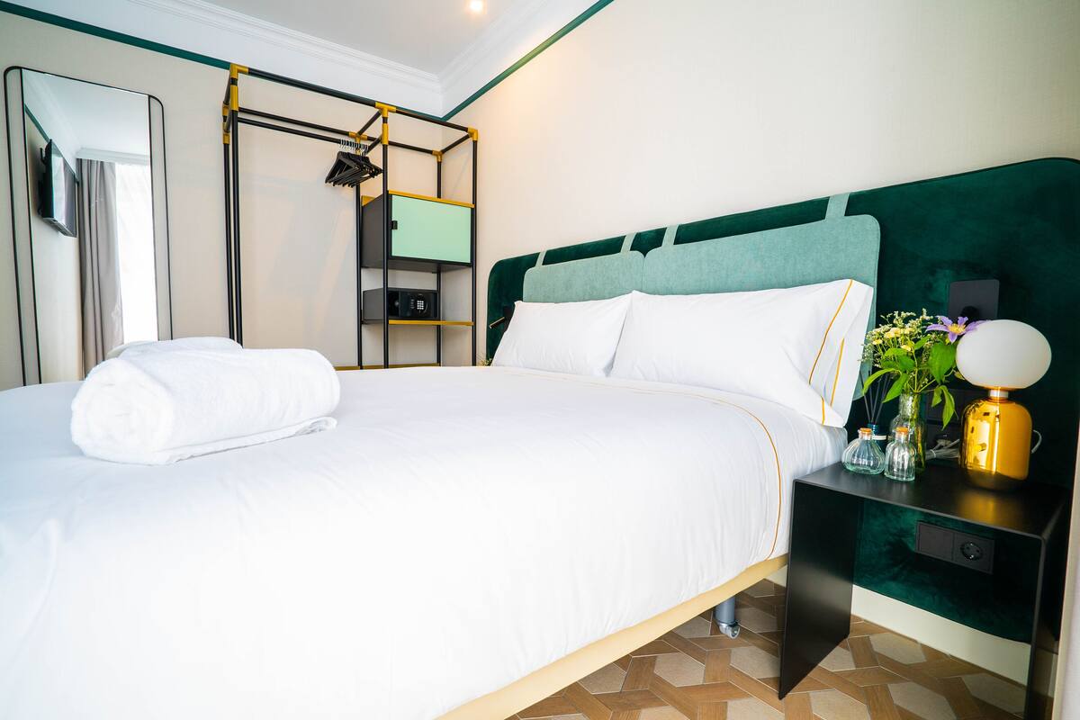 A neatly made bed with white linens, a bedside table with a lamp, and a mirror on the wall.