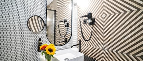Un baño con un lavamanos blanco, un espejo redondo y un secador de pelo de mano.