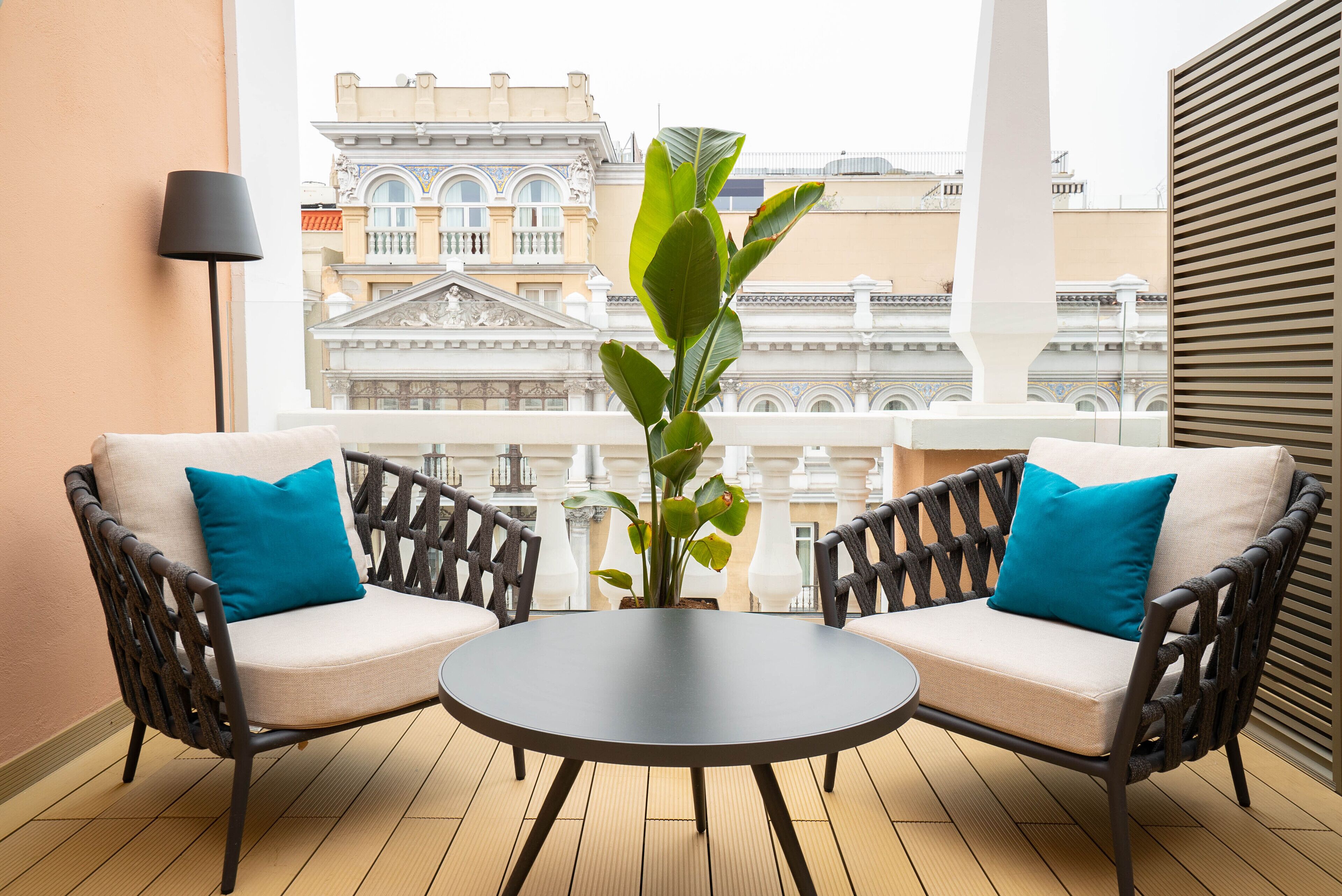 Ein Balkon mit zwei Korbstühlen, einem kleinen runden Tisch und einem Blumentopf.