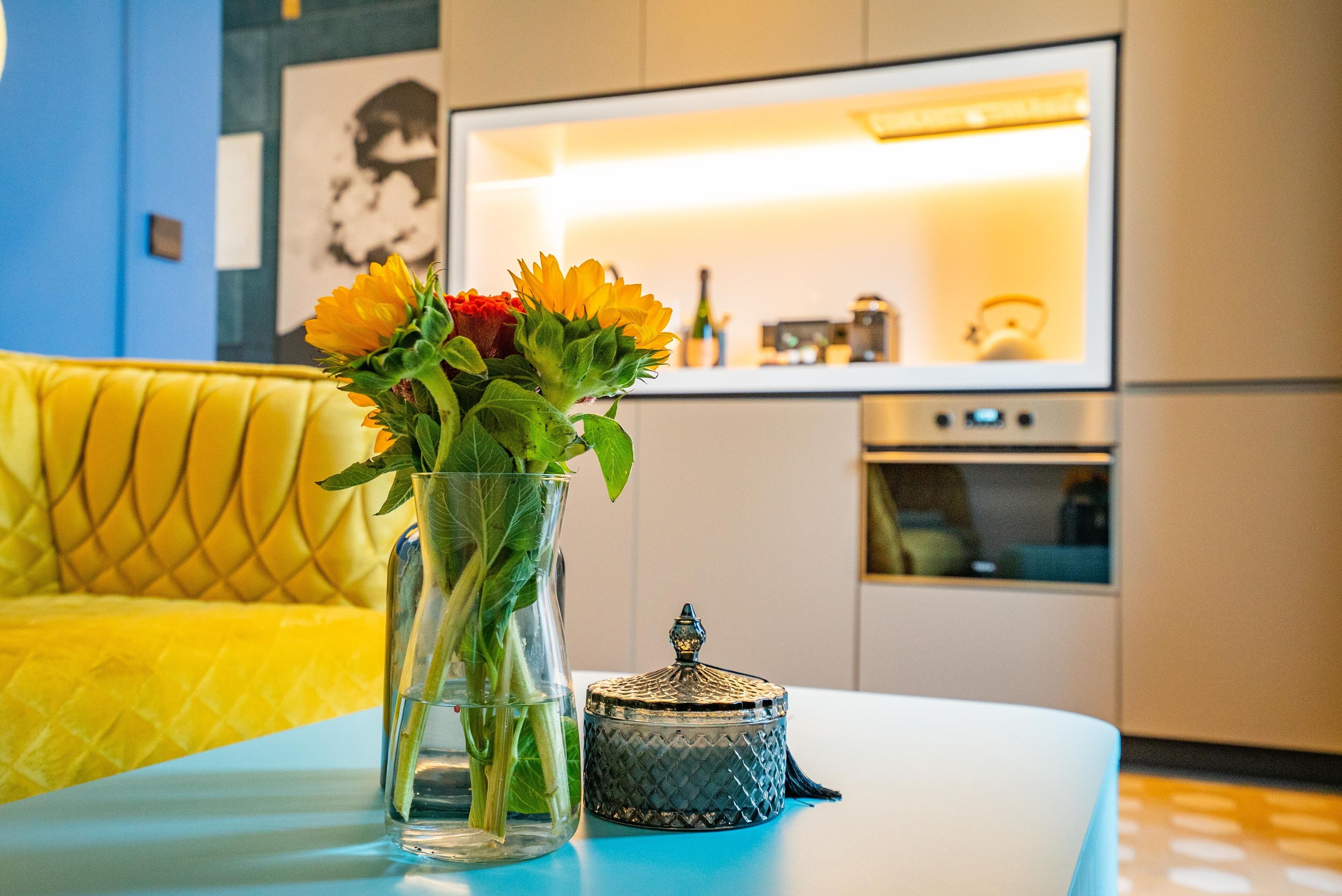 Eine moderne Küche mit Einbauofen und einem Essbereich, ausgestattet mit einem gelben Sofa und einem Tisch mit Blumen.