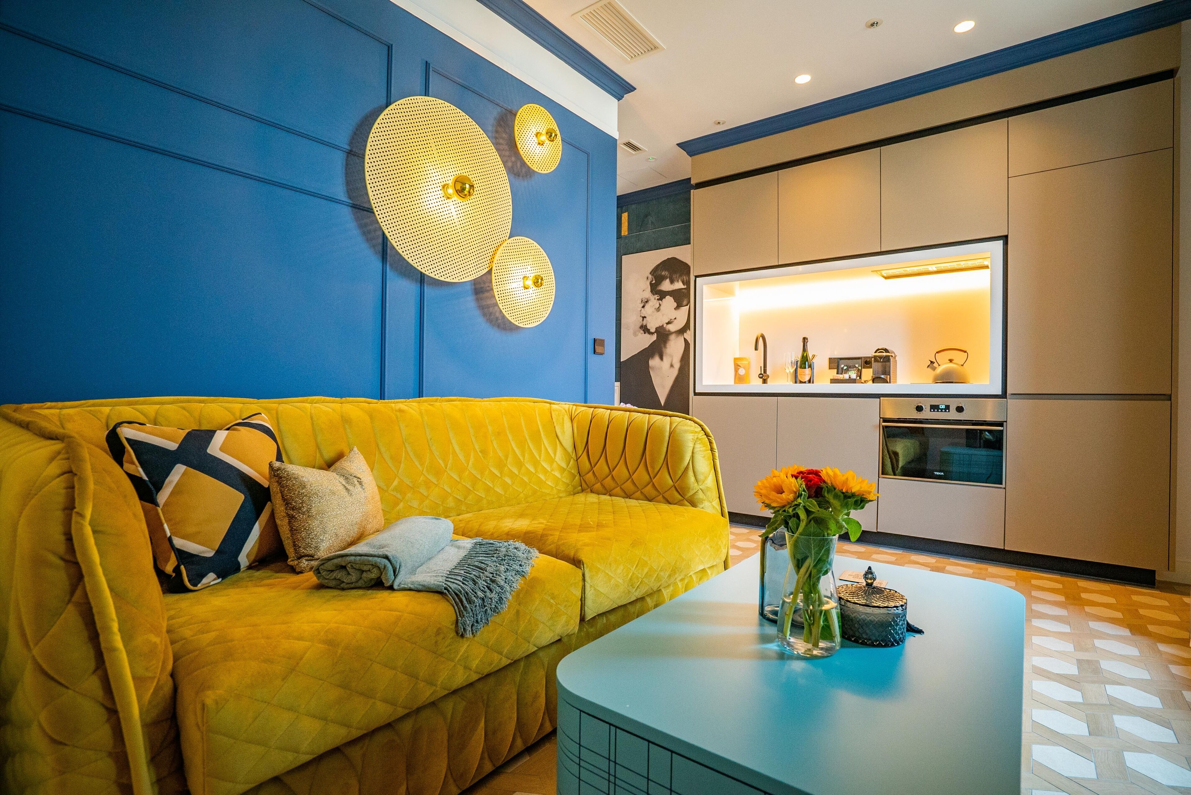 A modern living room with a yellow sofa, a blue coffee table, and decorative wall art.