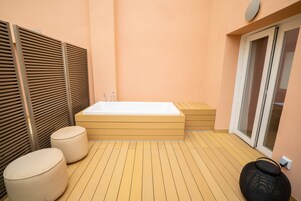 Ein modernes Badezimmer mit Holzboden, einer großen Badewanne und einer Glasdoor zu einem Außenbereich.