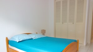 A single bed with a wooden frame and a blue mattress in a room with white walls and a tiled floor.