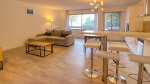 A modern living room with a sofa, a coffee table, and a dining area with bar stools.