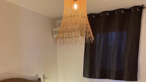 Et soveværelse med en seng, puder, en sengetavlelampe, en hængende lampe og et vindue med gardin.