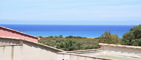 A coastal view from a building with a red roof, overlooking a beach and the sea.