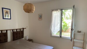 Un dormitorio con cama, mesita de noche, ventana con cortinas, estante en la pared y lámpara colgante.