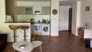 Una cocina moderna con microondas, horno y lavadora. Hay dos taburetes de madera y una pequeña mesa con una revista.