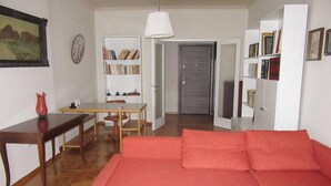 A living room with a wooden floor, a red sofa, a wooden coffee table, a dining table with chairs, a bookshelf, and a door leading to another room. - 2 Bed Flat - Sleeps 4 - Pets - Wifi (Thessaloniki)