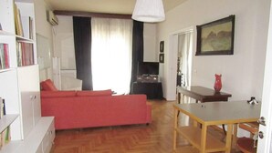 A living room with a red sofa, a wooden dining table, and a bookshelf. - 2 Bed Flat - Sleeps 4 - Pets - Wifi (Thessaloniki)