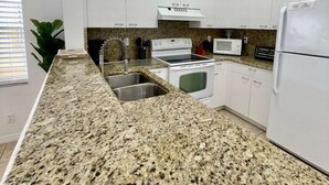 Une cuisine moderne avec des armoires blanches, des comptoirs en granit, un évier en acier inoxydable, une cuisinière, un four à micro-ondes et un réfrigérateur.