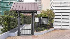 Una entrada protegida por un portón, con una estructura metálica de techo y una valla de metal, y un edificio con fachada blanca y líneas horizontales.