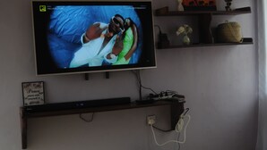 A television mounted on a wall, with a shelf above it holding decorative items. - Hakuna Matata Cozy Apartment (Karatu)