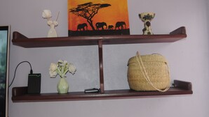 A shelf with a painting, a vase with flowers, a woven bag, and a small electronic device. - Hakuna Matata Cozy Apartment (Karatu)