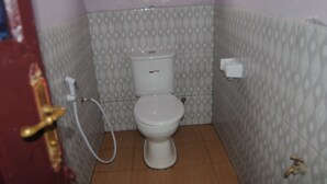 A small bathroom with a toilet, a toilet paper holder, and a door with a brass handle. - Hakuna Matata Cozy Apartment (Karatu)