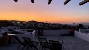A rooftop terrace with a sunset view, featuring a seating area with chairs and a table, potted plants, and a cityscape in the background. - Charming Private Greek Heritage Retreat (Tavros) (Mykonos-Town)