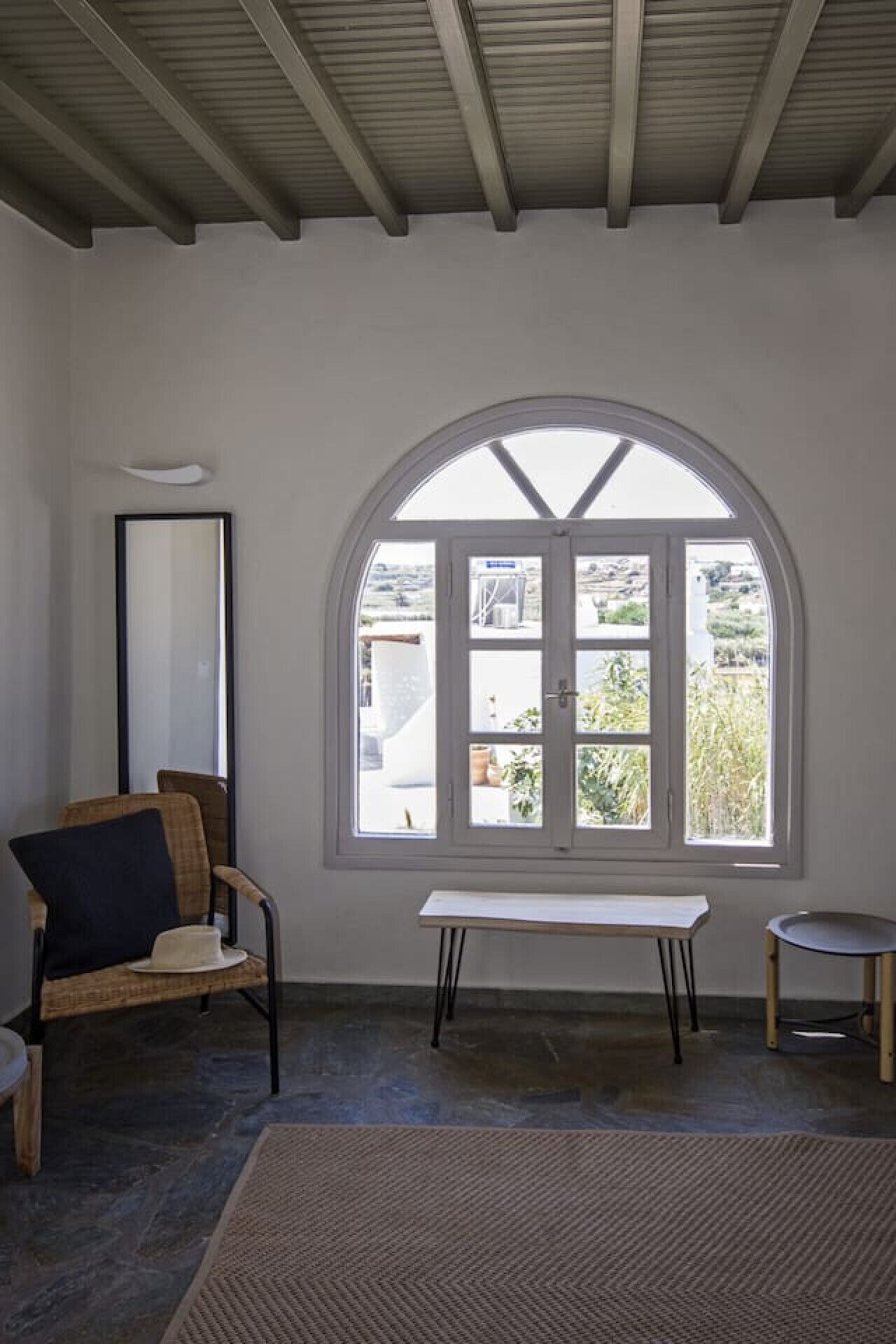 A room with a large arched window, a bench, a chair, and a small table.