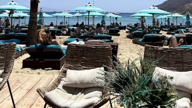 A beachside lounge area with wicker lounge chairs and blue umbrellas, overlooking the sea. - Charming Private Greek Heritage Retreat (Tavros) (Mykonos-Town)