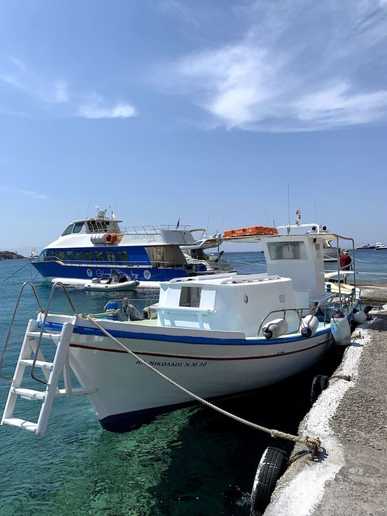 A docked boat with a ladder and a smaller boat nearby.