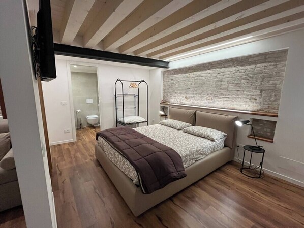 Une chambre à coucher avec un lit, un plafond en bois, un mur en pierre et une petite table de chevet avec une lampe.