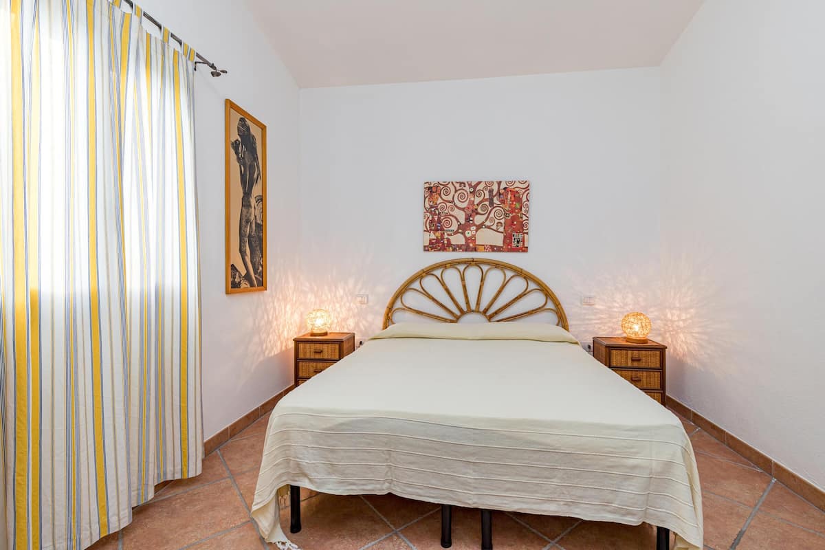 Une chambre à coucher comprenant un lit, deux tables de chevet, un rideau et deux lampes fixées au mur.
