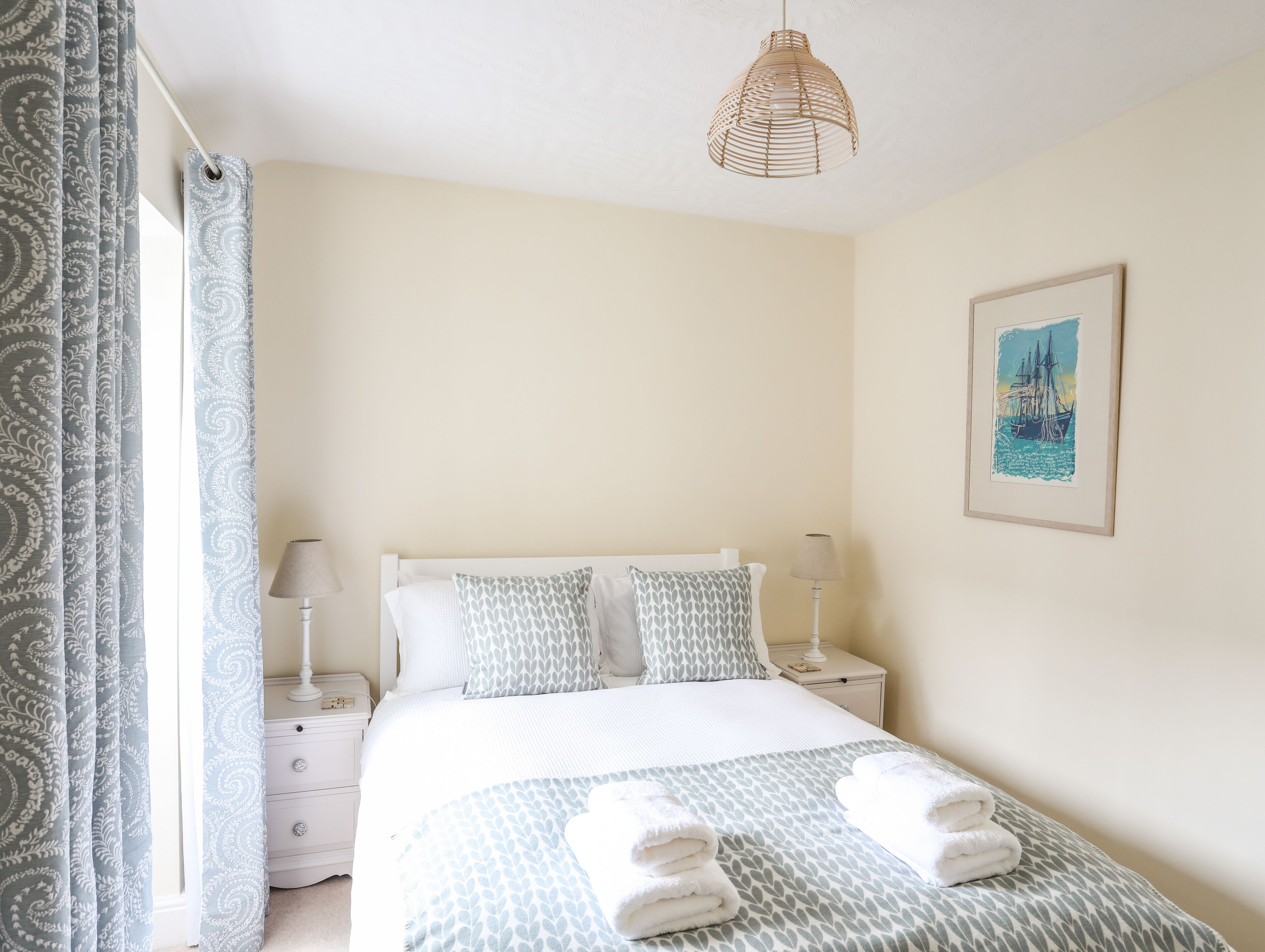 A neatly arranged bedroom with a bed, bedside tables, a lamp, and a painting on the wall.