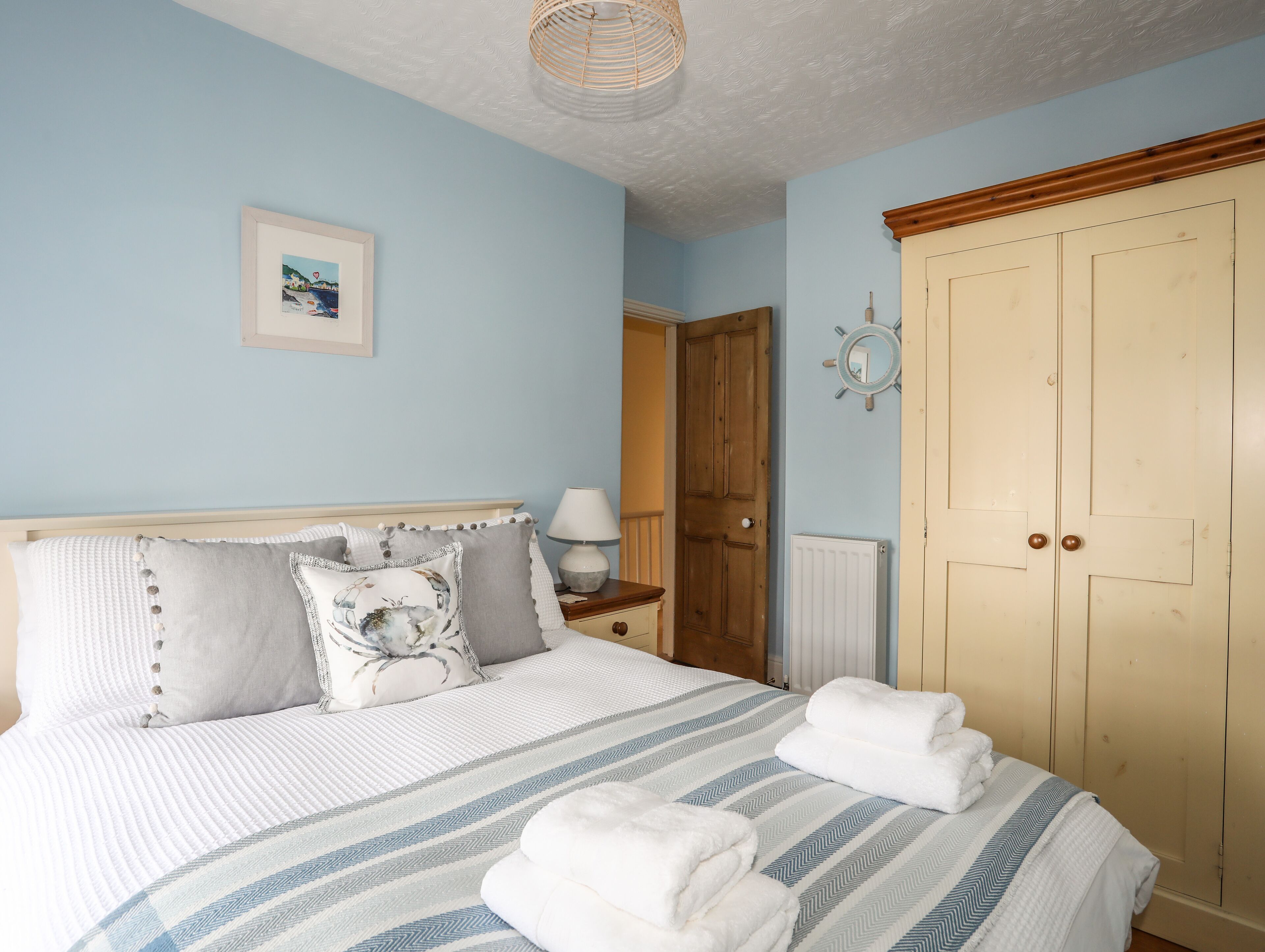 Une chambre à coucher comprenant un lit, des oreillers, une table de chevet avec une lampe, une armoire et un miroir fixé au mur.